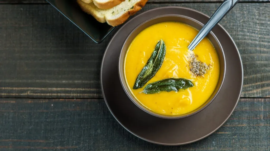 Butternut squash soup with sage leaves in brown ceramic soup plate with garlic bread