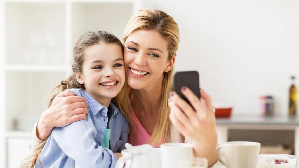 happy mother and daughter with smartphone having breakfast