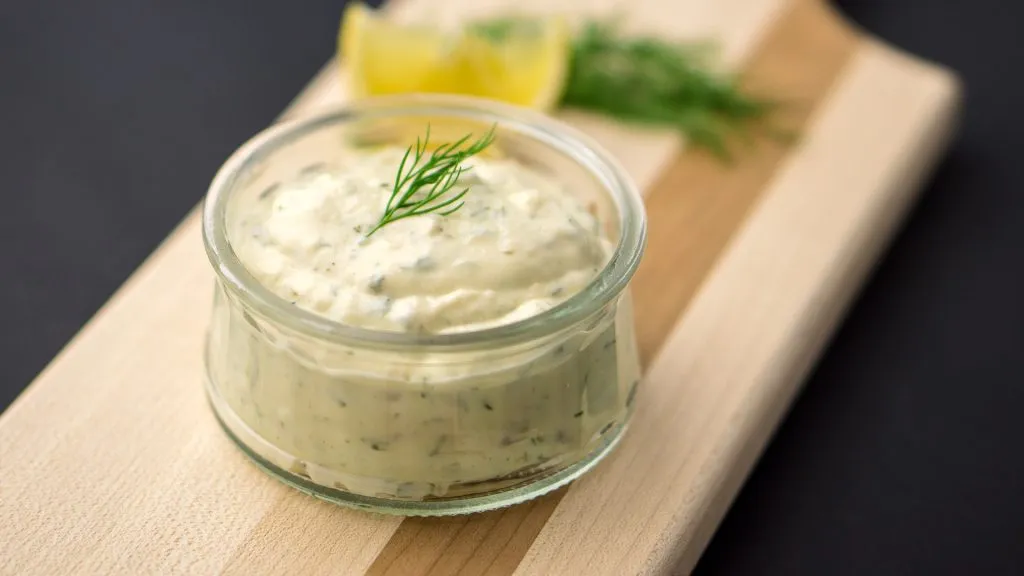 tartar sauce on a cutting board with a lemon slice and dill