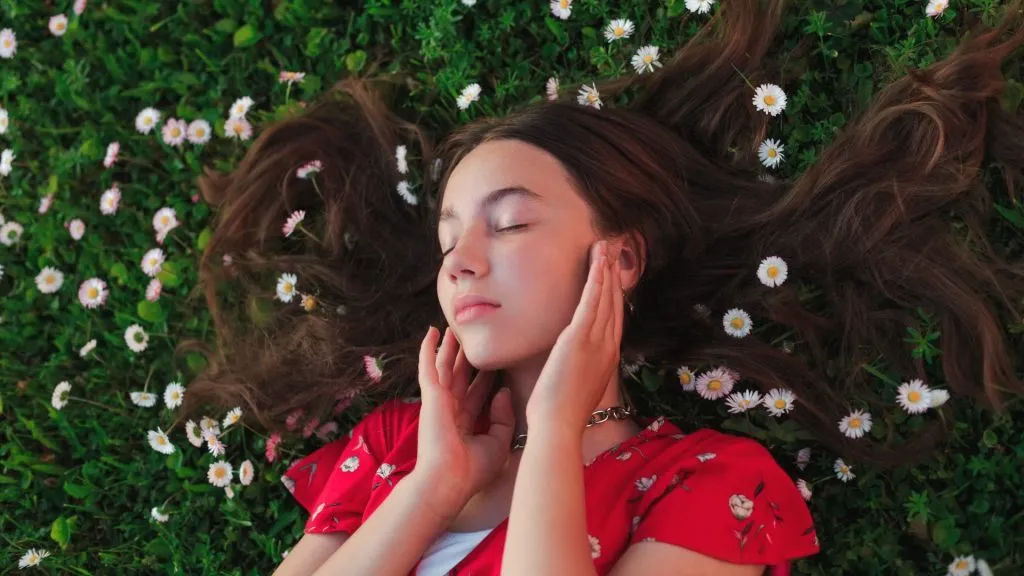 Young woman lying on the grass with daisies and closed eyes tips for naturally soft skin.