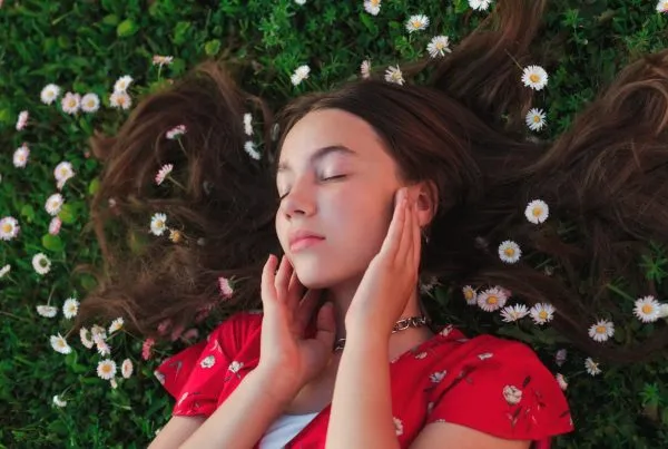 Young woman lying on the grass with daisies and closed eyes tips for naturally soft skin.