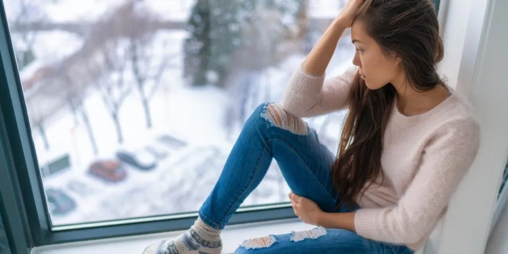 Winter depressed sad girl lonely sitting near window looking at cold weather. Upset or unhappy.