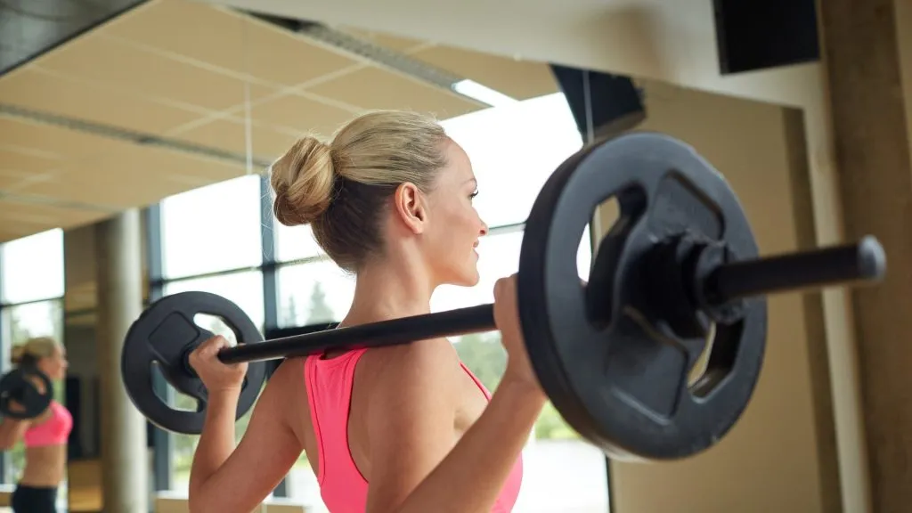 Blonde woman lifting large free weights from back