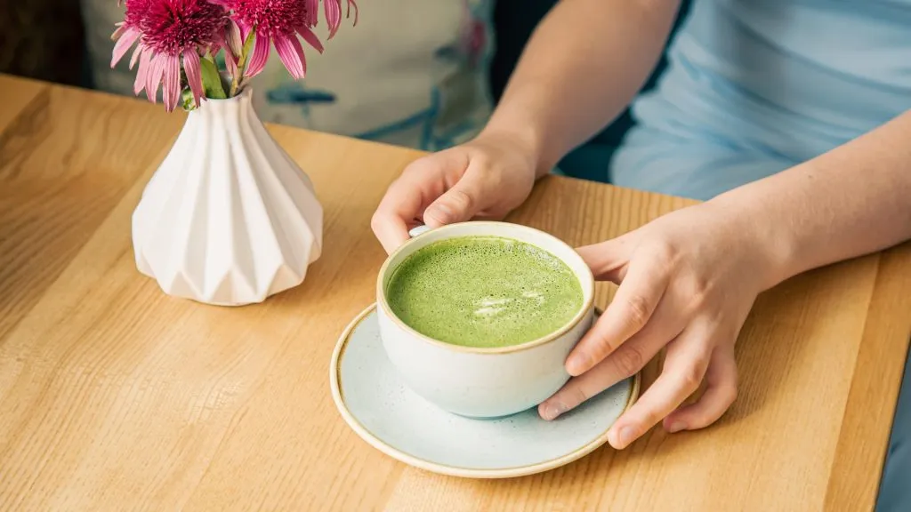 Woman's hands holding a cup of matcha latte in cafe