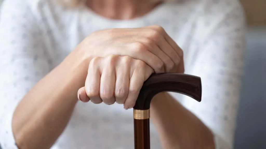 Close up older woman holding wrinkled hands on wooden cane