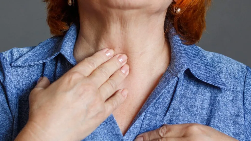An elderly woman feels her thyroid gland. Thyroid nodules