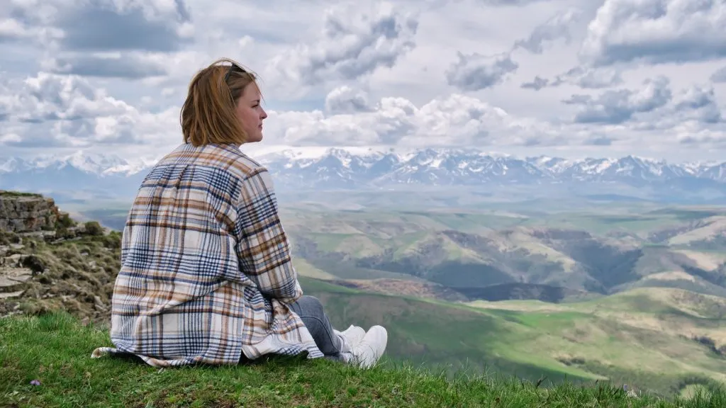Woman sitting on top a hill with clouds gazing into the distance