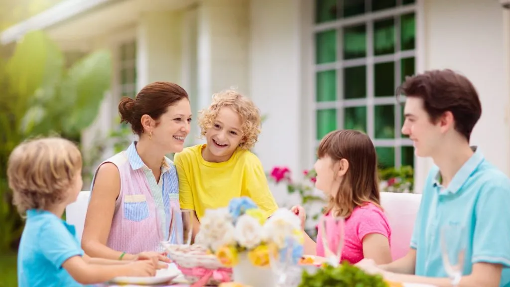 Family eating outdoors. Garden summer or spring fun. Barbecue in sunny backyard. Mother's day or Easter celebration. Kids eat lunch in outdoor deck in pastel colors. Parents and children enjoy bbq. Local events