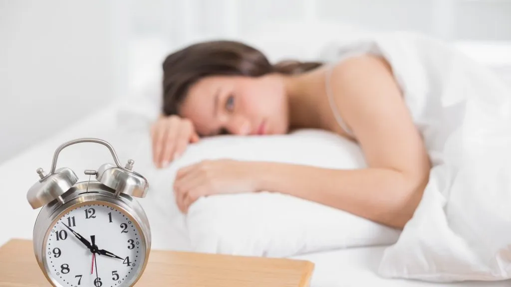 Woman in bed, not sleeping, looking at alarm clock