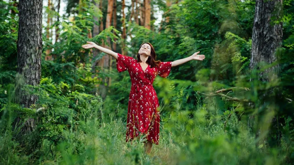 Young woman in a red dress in the summer forest. A girl in a red dress walks through the forest.