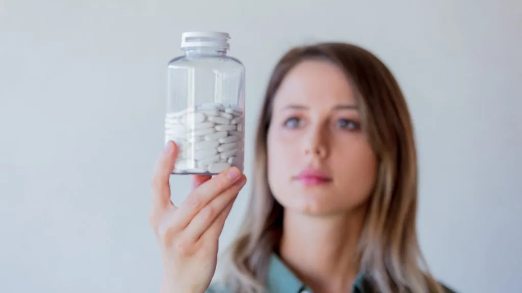 Young woman holding a jar of pills. Focus on the bottle.