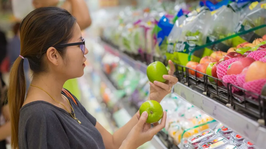 Young Asian woman shopping for fruits at the grocery store or supermarket. Is organic better?
