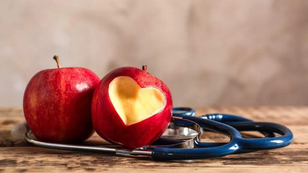 Red apples and stethoscope on wooden table