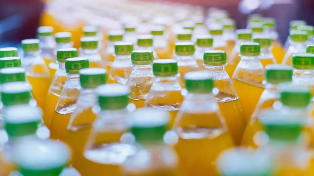 Close up of plastic bottles of orange soda on conveyor belt.