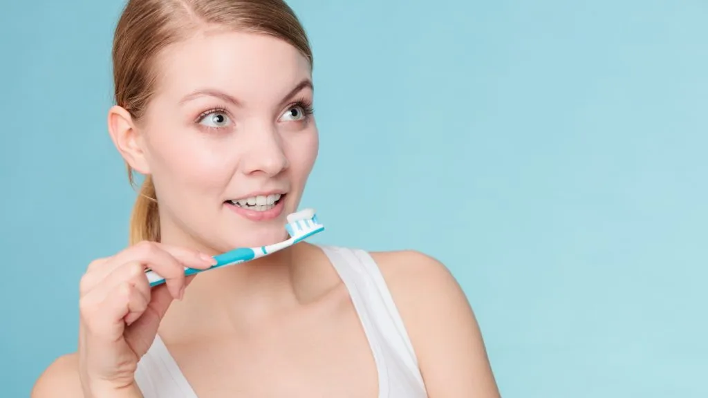 Young woman brushing cleaning teeth. Girl holds toothbrush with toothpaste on it.
