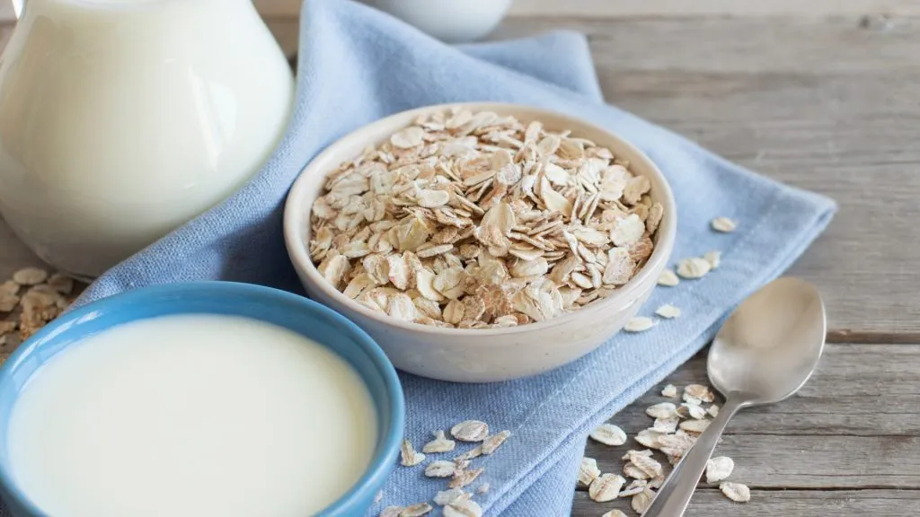 Rolled oats in a bowl and milk on a wooden table